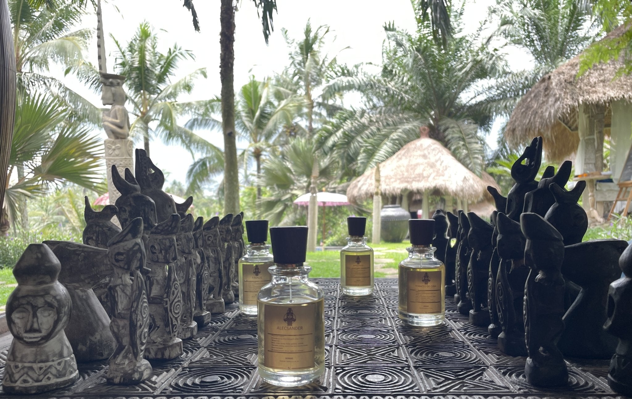 Image on the About Us page showcasing Nomad perfume bottles arranged on a chessboard against a backdrop of tropical nature, blending sophistication with the allure of lush surroundings